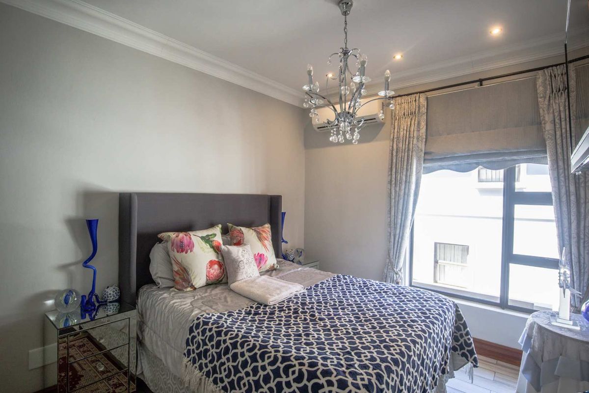 A well-maintained bedroom featuring crown molding, a split-system air conditioning unit, and large windows with fitted curtains.
