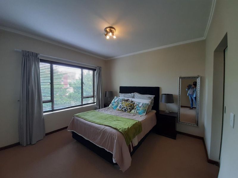 A well-lit bedroom featuring neutral walls, carpeted flooring, and a large window with venetian blinds, providing a comfortable and functional living space.