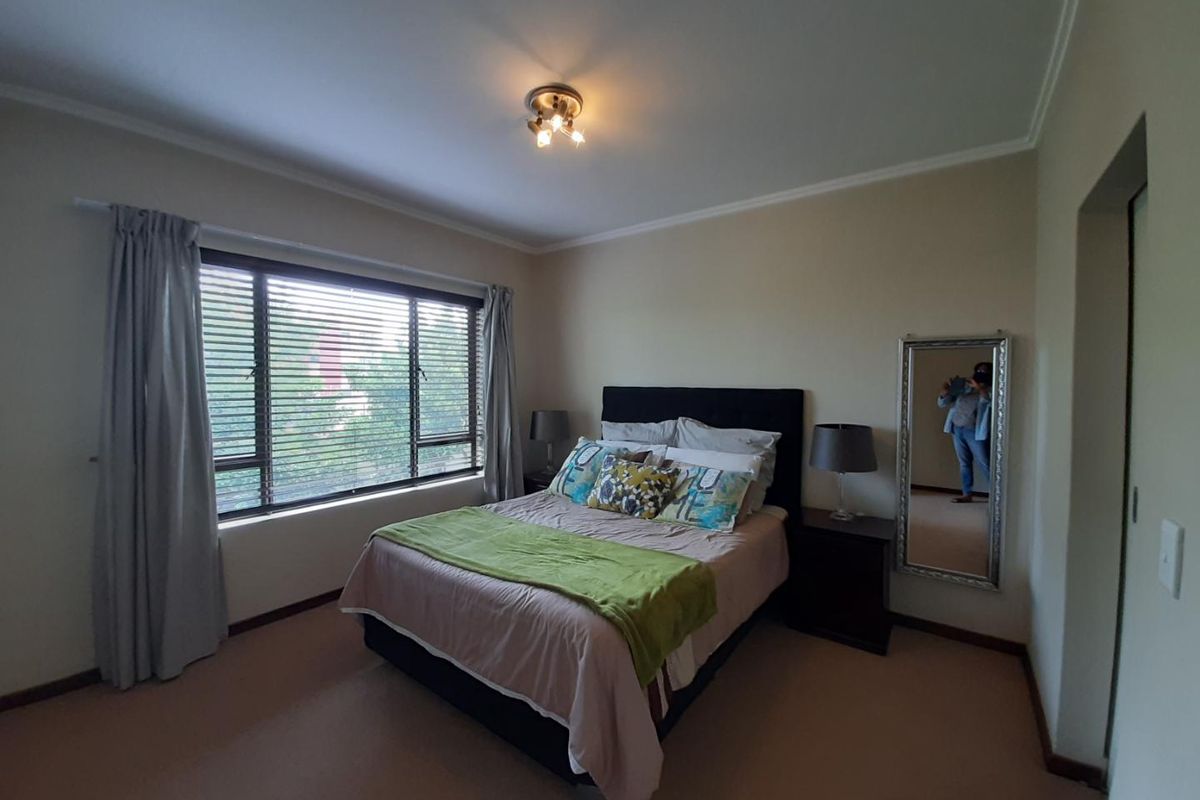 A well-lit bedroom featuring neutral walls, carpeted flooring, and a large window with venetian blinds, providing a comfortable and functional living space.