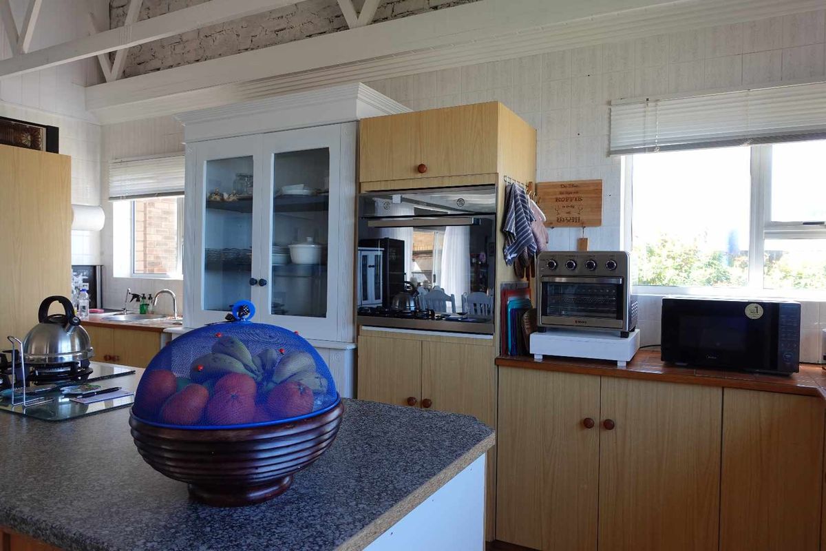 A functional kitchen featuring light wood cabinetry, laminate countertops, a built-in oven, and exposed white-painted roof trusses, offering a bright and practical workspace.