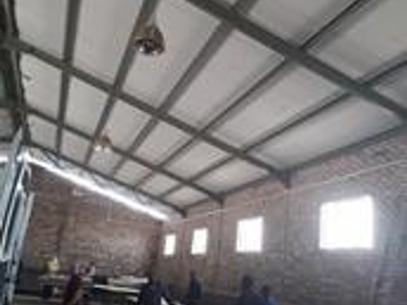 Spacious industrial utility area featuring exposed steel roof trusses, brick walls, and concrete flooring, suitable for workshop or storage use.