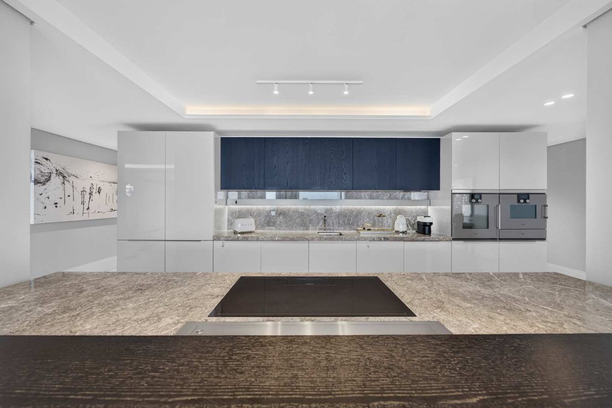 Modern kitchen featuring high-end stone countertops, integrated cabinetry, a sleek induction cooktop, and built-in double ovens with sophisticated under-cabinet lighting.