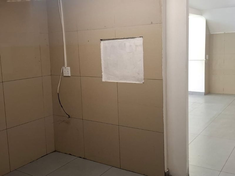 An empty utility or service area featuring tiled walls and flooring, with visible electrical points and an unfinished wall section.