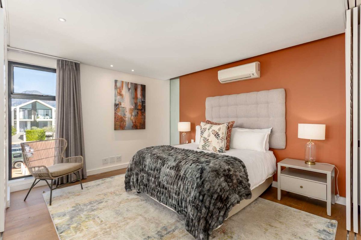A well-maintained bedroom featuring timber flooring, recessed lighting, a split-system air conditioner, and a large window with natural light.