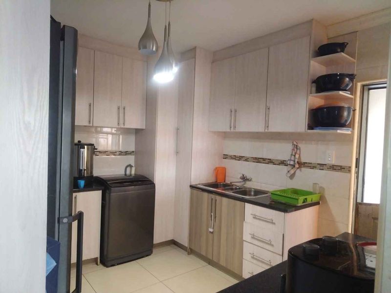 A functional kitchen featuring light-toned built-in cabinetry, a double bowl sink, tiled backsplash, and modern pendant lighting.