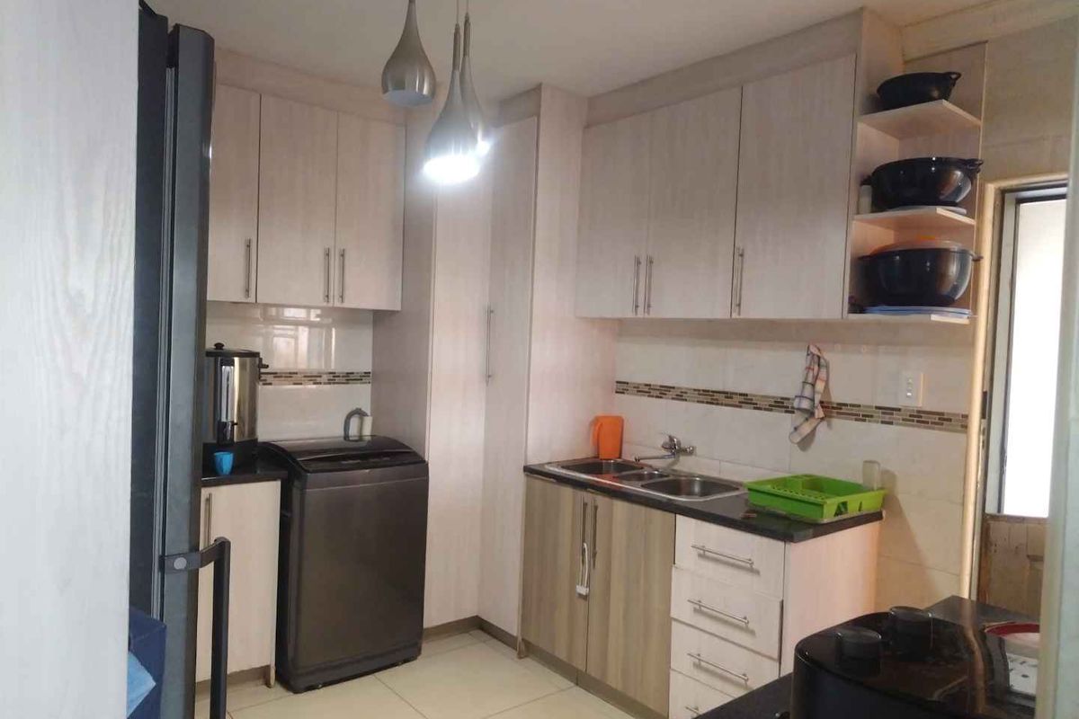 A functional kitchen featuring light-toned built-in cabinetry, a double bowl sink, tiled backsplash, and modern pendant lighting.
