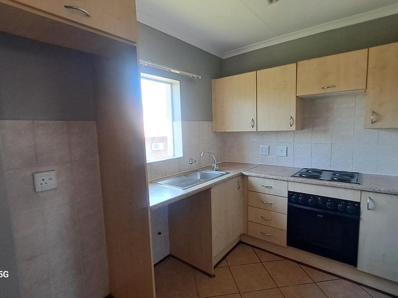 A functional kitchen featuring light wood-finish cabinetry, laminate countertops, a built-in oven with electric hob, and tiled flooring.