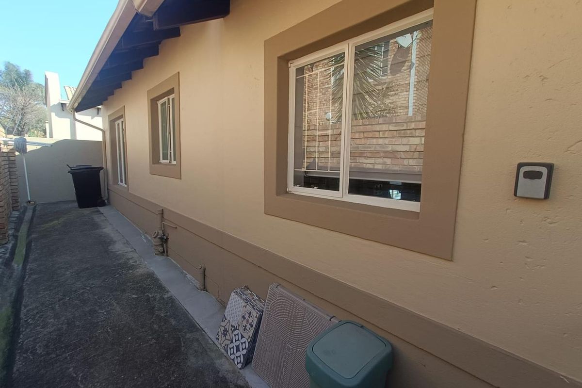 A view of the rear exterior wall of the townhouse, featuring sliding windows, exposed rafters, and a concrete pathway along the side of the building.
