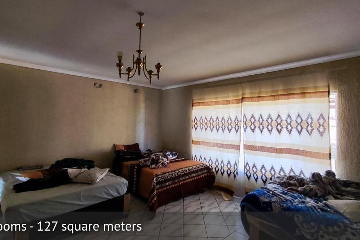 A spacious bedroom featuring tiled flooring, a central chandelier, and large windows with patterned curtains.