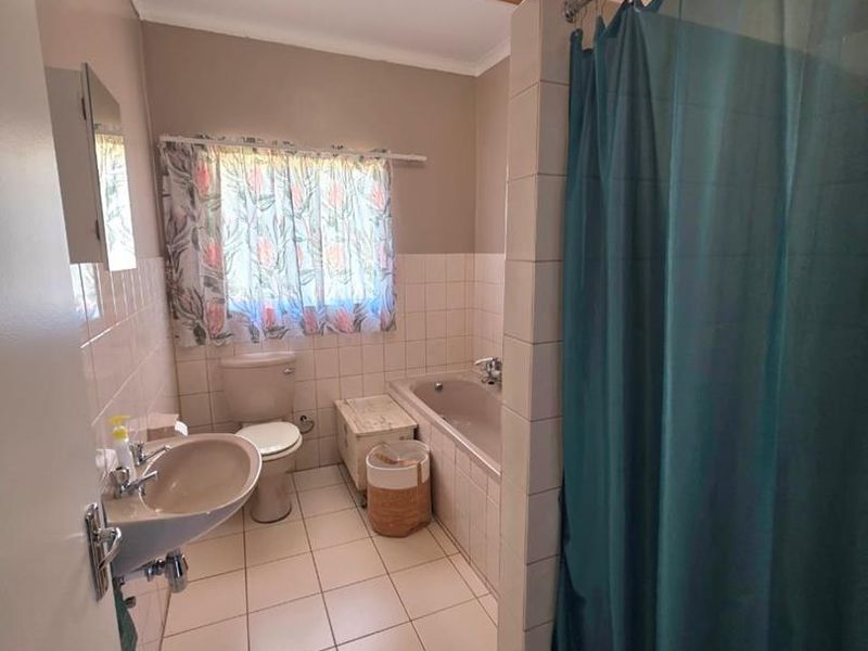 A functional bathroom featuring a bathtub, pedestal basin, and toilet with neutral wall and floor tiling.