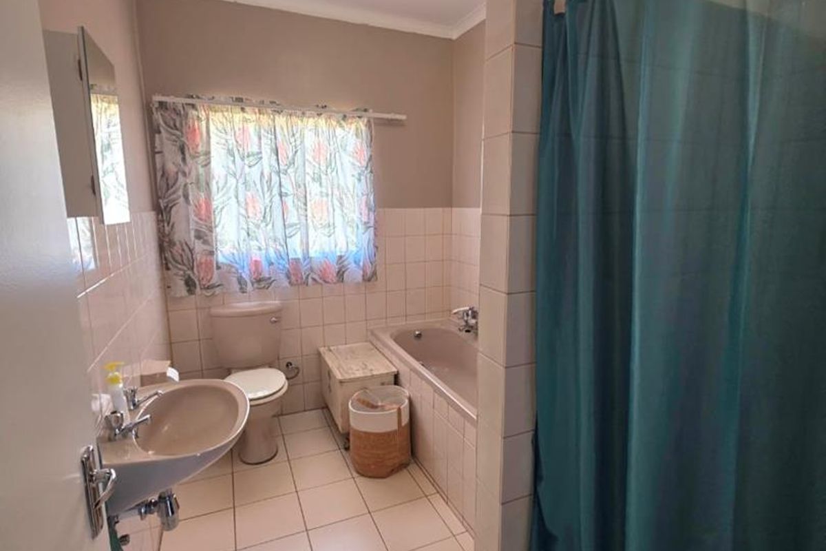 A functional bathroom featuring a bathtub, pedestal basin, and toilet with neutral wall and floor tiling.