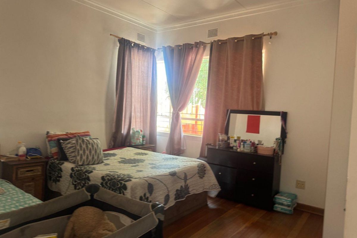 A bedroom featuring wooden flooring, large windows with curtain rods, and crown molding, providing a functional space for rest.