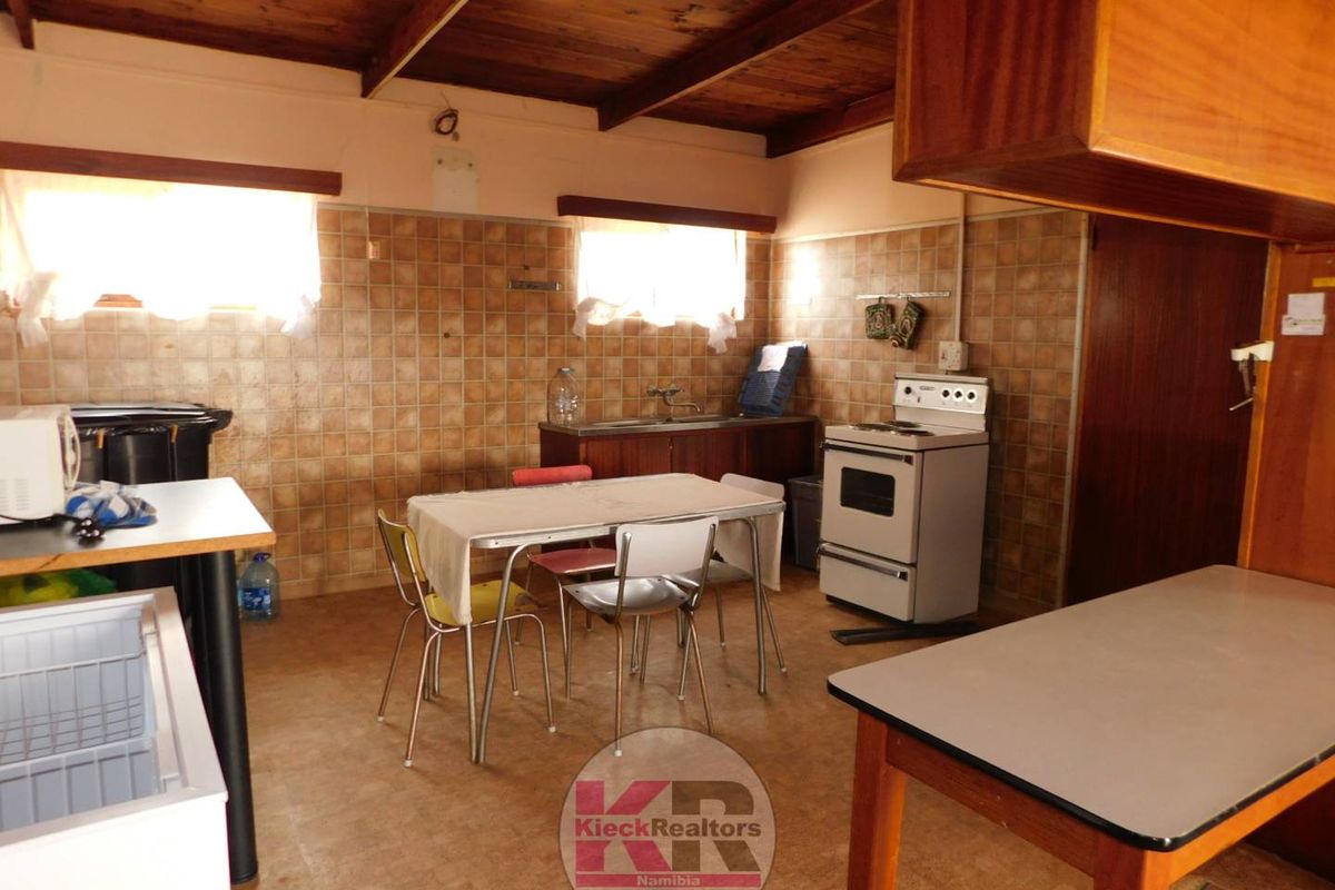 A dated kitchen featuring tiled walls, timber ceiling beams, and a freestanding stove, offering a functional space with potential for modernization.