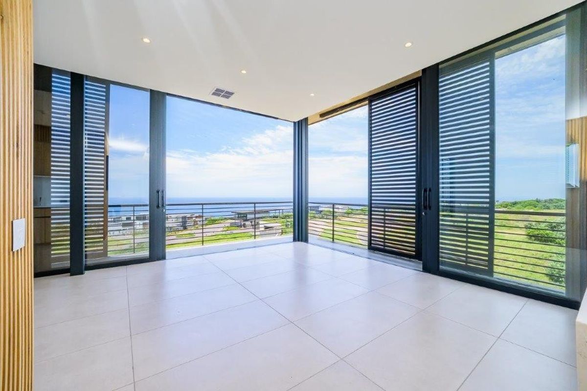 A bright, modern living area featuring large format floor tiles, timber slat accents, and expansive sliding glass doors opening to a scenic balcony.