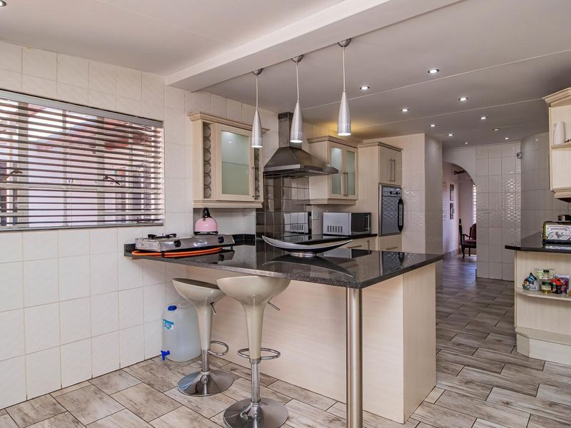 A functional kitchen featuring granite countertops, built-in cabinetry, a breakfast bar, and modern stainless steel appliances with tiled finishes throughout.