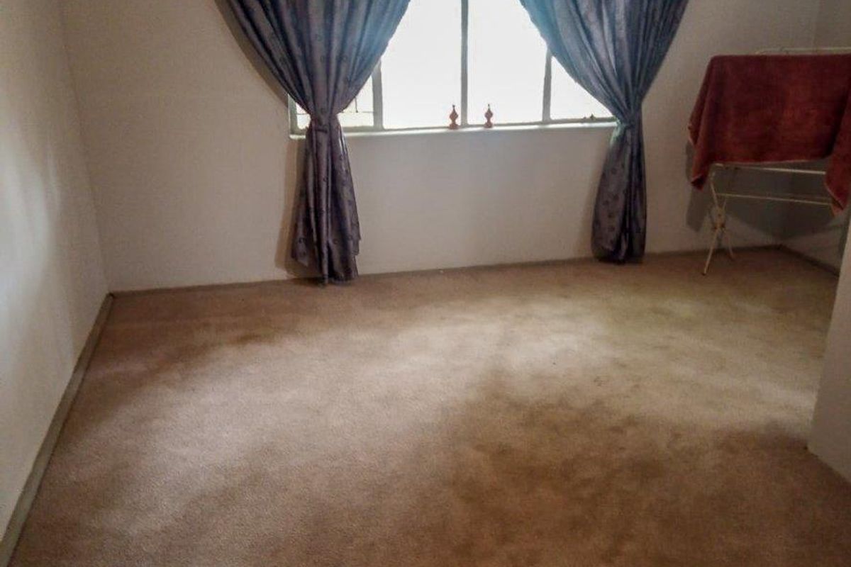 A vacant bedroom featuring neutral wall finishes, fitted carpeting, and a window with installed curtain rails.