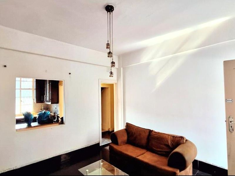 A living room featuring a kitchen pass-through window, pendant lighting, and neutral wall finishes, providing a functional and connected living space.
