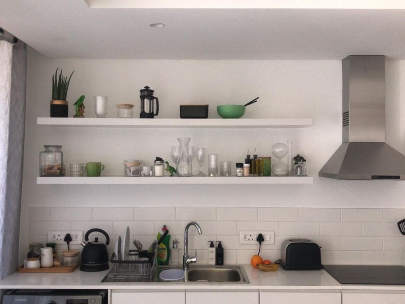 Modern kitchen featuring white cabinetry, subway tile backsplash, floating shelves, stainless steel extractor fan, and an integrated induction cooktop.
