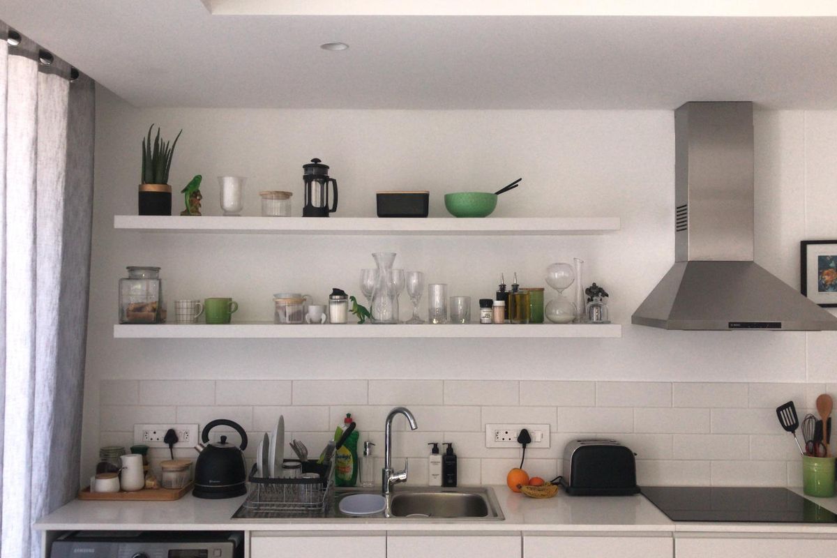 Modern kitchen featuring white cabinetry, subway tile backsplash, floating shelves, stainless steel extractor fan, and an integrated induction cooktop.