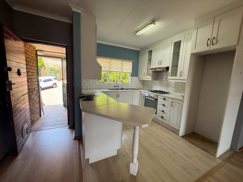 A functional kitchen featuring white cabinetry, subway tile backsplash, built-in oven, gas hob, and a breakfast bar, with direct access to the exterior.