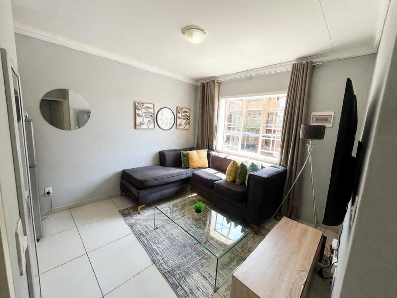 A well-maintained living room featuring neutral tiled flooring, a large window allowing natural light, and clean wall finishes.