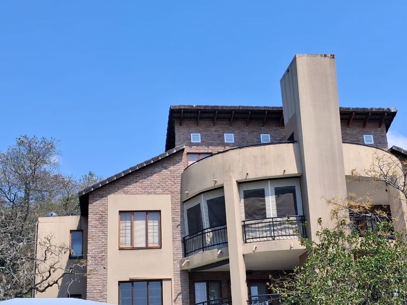 Rear elevation of a multi-story apartment building featuring brick and stucco facade, curved balconies with metal railings, and a prominent chimney stack.
