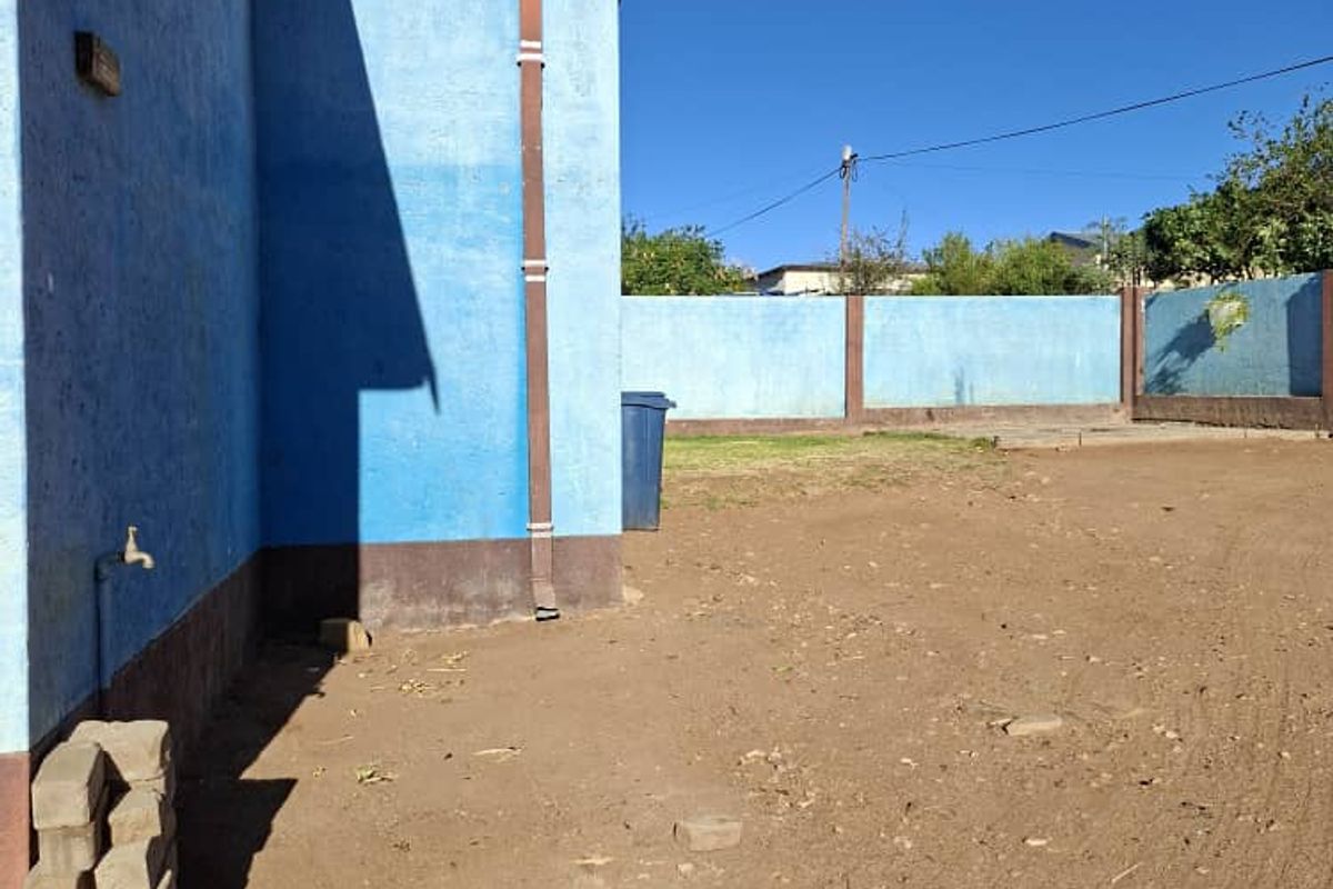 A view of the rear exterior of the property featuring a blue painted wall, downpipe, and an open, unpaved backyard area.