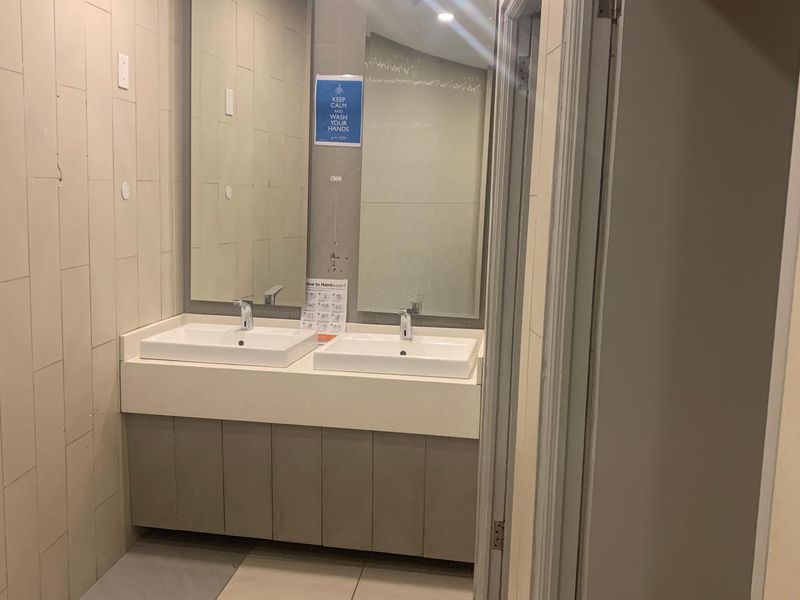 A functional office bathroom featuring a double vanity with ceramic basins, chrome faucets, and tiled wall finishes.