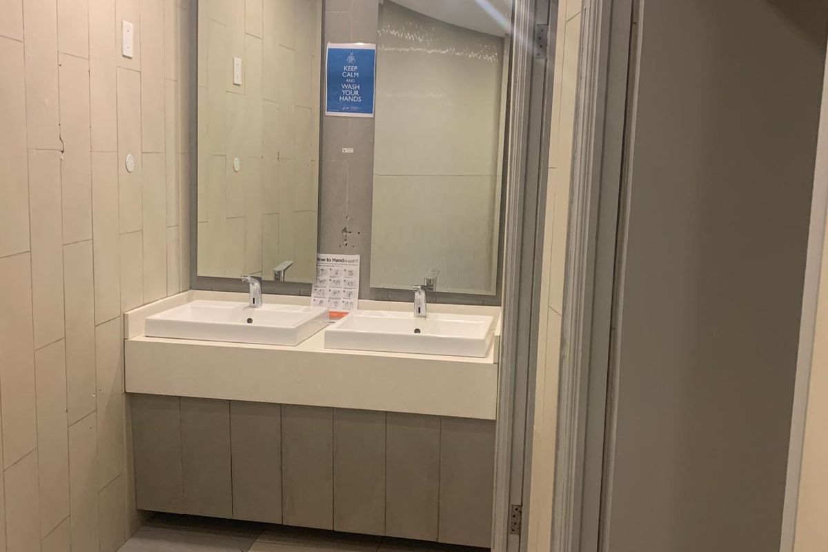 A functional office bathroom featuring a double vanity with ceramic basins, chrome faucets, and tiled wall finishes.