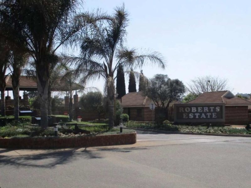 The entrance to Roberts Estate featuring a secure gatehouse, brick boundary walls, and well-maintained landscaped gardens.