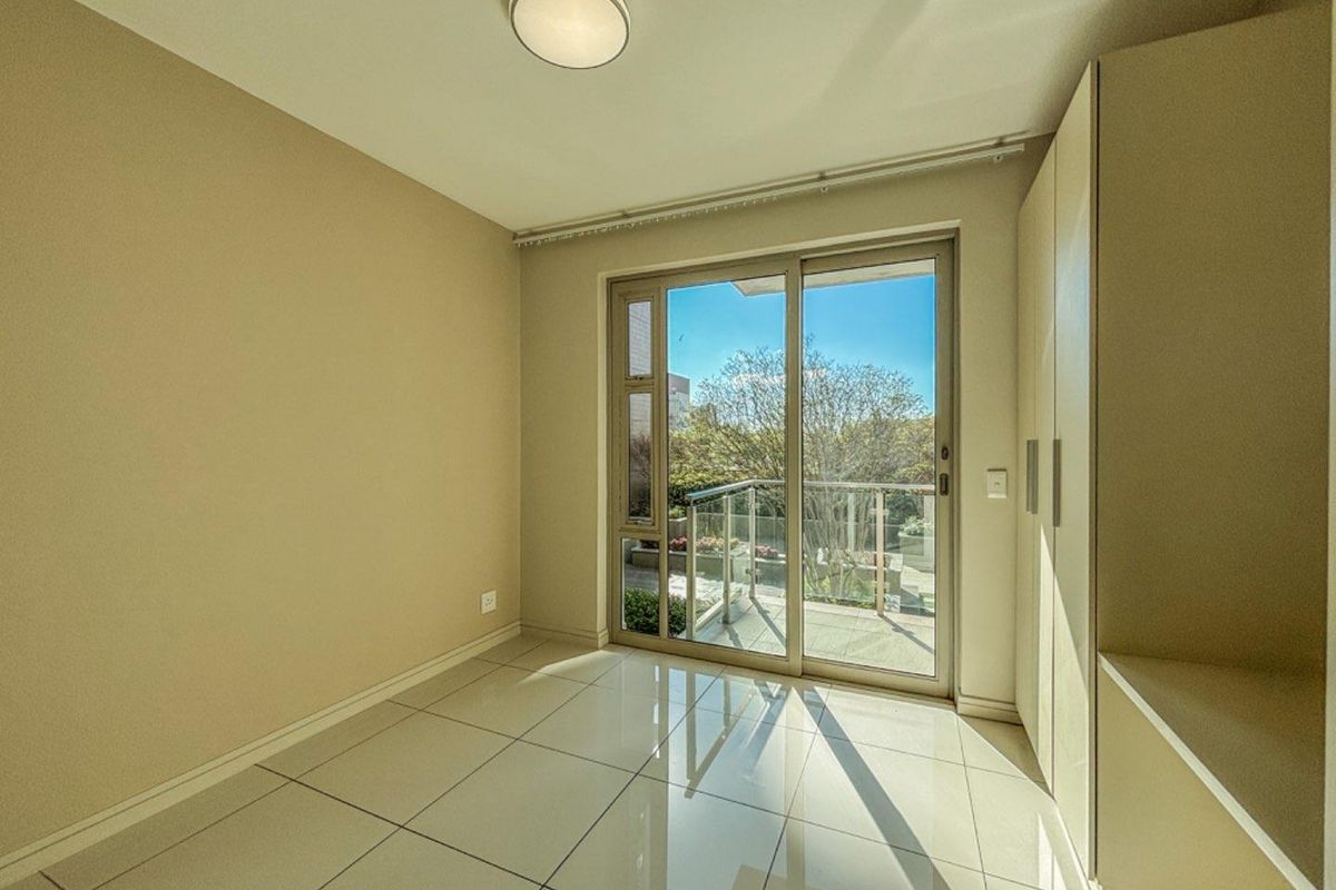 A bright, empty bedroom featuring neutral tiled flooring, built-in cabinetry, and sliding glass doors that open onto a private balcony.