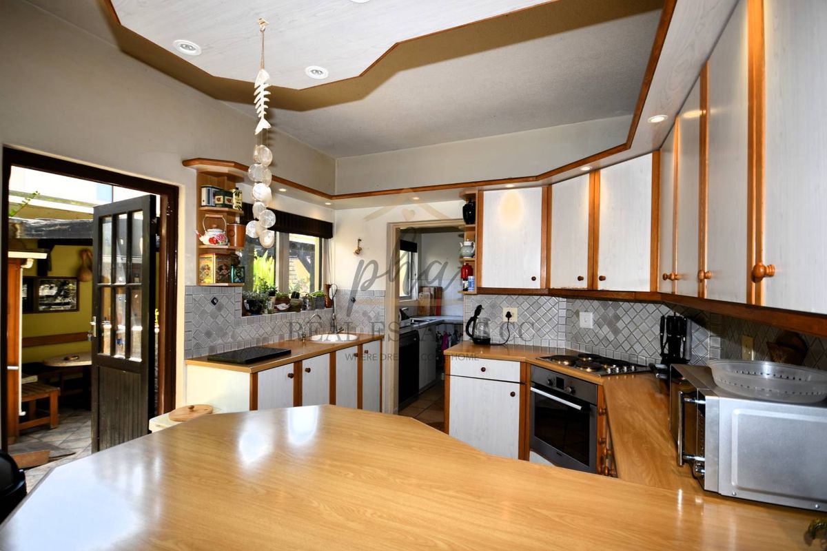 A functional kitchen featuring wooden cabinetry, integrated gas hob, built-in oven, and a breakfast bar, with direct access to an outdoor patio area.