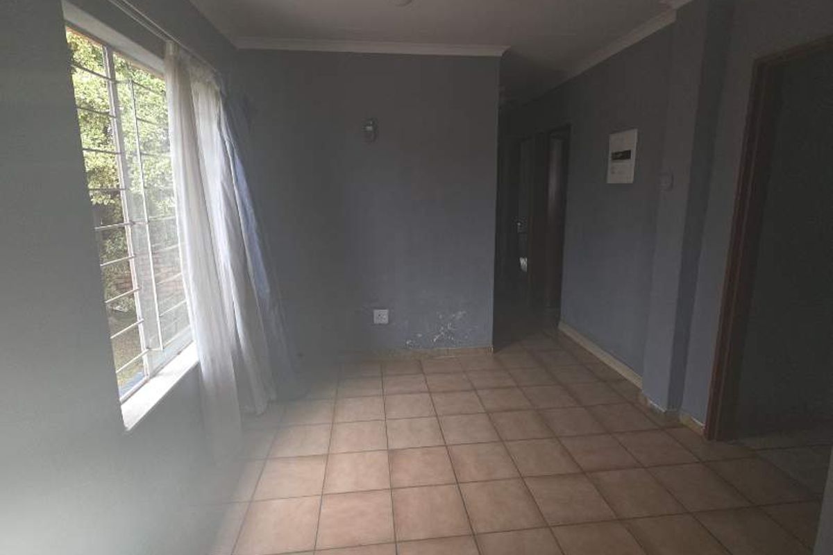 An empty living area featuring tiled flooring, grey painted walls, and a window with security bars.
