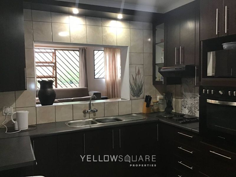 A functional kitchen featuring dark wood cabinetry, built-in oven, hob, extractor fan, and a convenient pass-through window overlooking the living area.