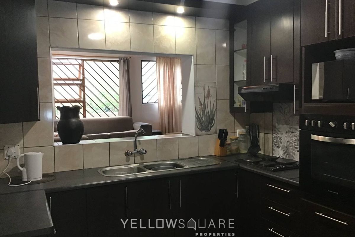 A functional kitchen featuring dark wood cabinetry, built-in oven, hob, extractor fan, and a convenient pass-through window overlooking the living area.