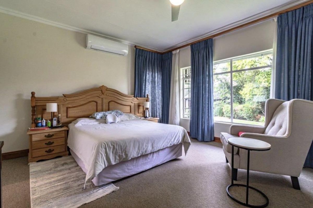 Spacious bedroom featuring large windows with garden views, carpeted flooring, crown molding, and a wall-mounted air conditioning unit.