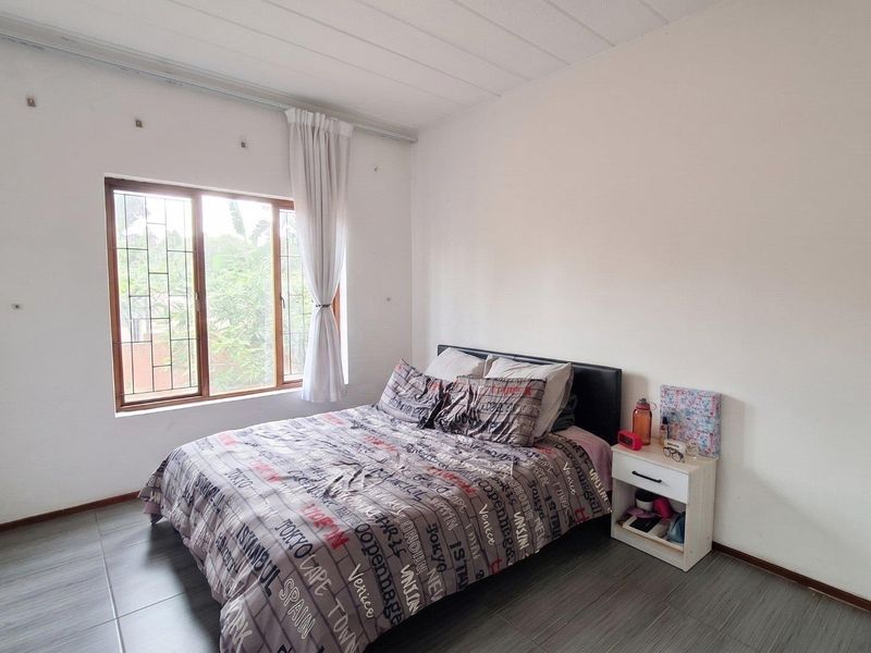 A bedroom featuring tiled flooring, a window with security bars, and neutral wall finishes, offering a functional space ready for personalization.