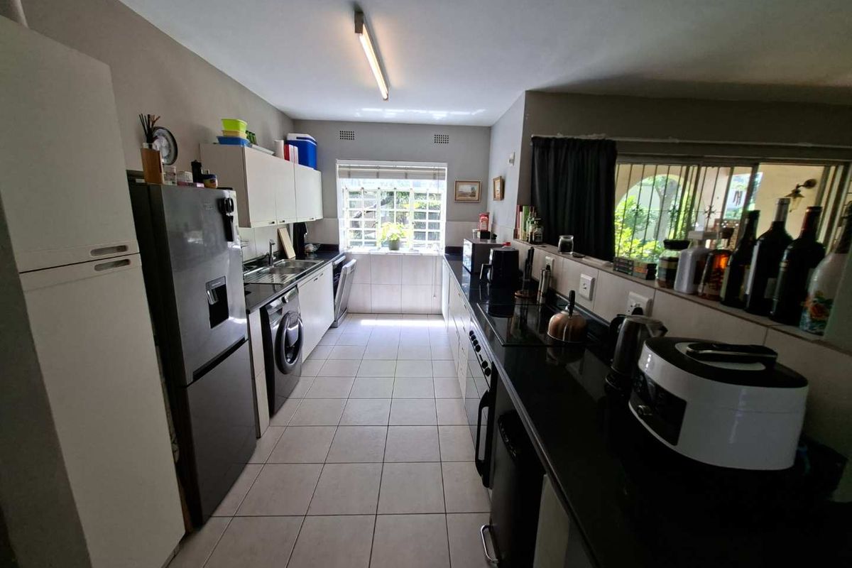A functional galley-style kitchen featuring dark granite countertops, ample built-in cabinetry, and tiled flooring with natural light from the rear window.