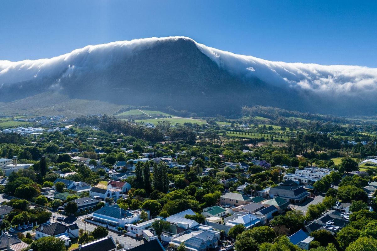 An aerial view of the residential neighborhood and surrounding landscape, featuring a prominent mountain backdrop with cloud cover.