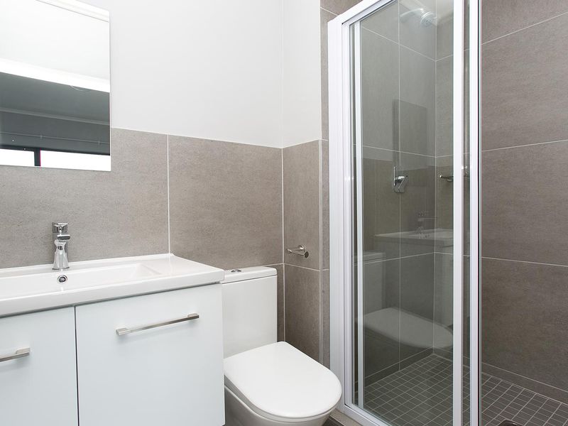 Modern bathroom featuring a vanity cabinet with basin, dual-flush toilet, and a glass-enclosed shower with neutral ceramic tiling.