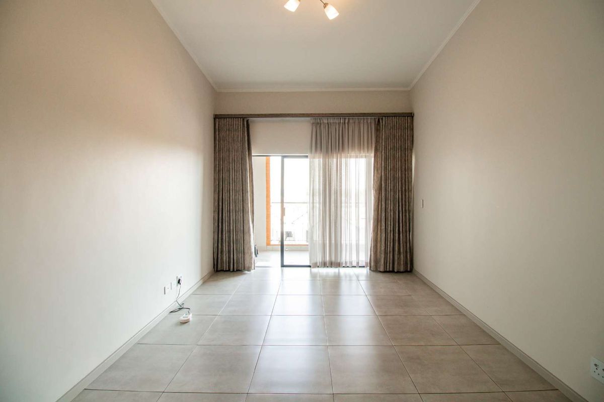 A bright, empty living room featuring neutral floor tiles, clean walls, and sliding glass doors leading to an outdoor balcony area.