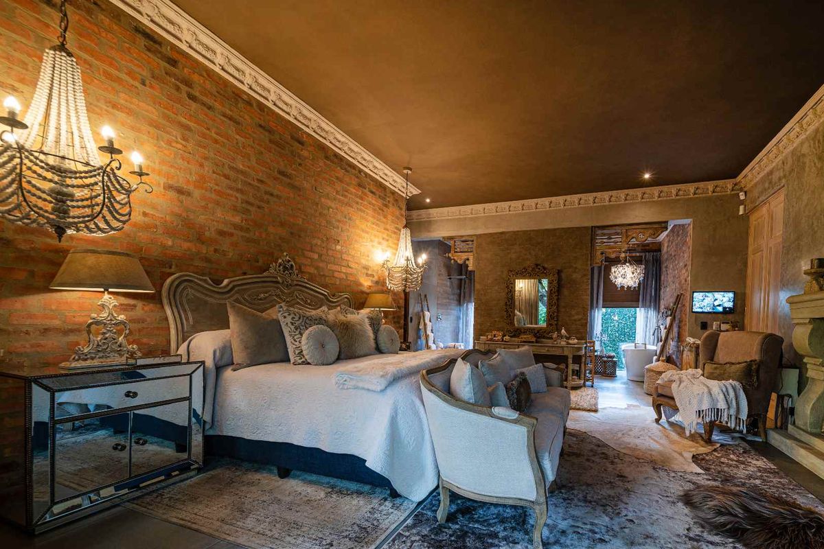 Spacious bedroom featuring exposed brick walls, ornate crown molding, and a warm, rustic aesthetic with integrated lighting and high-end finishes.