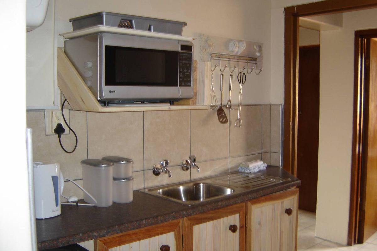 A functional kitchen area featuring a stainless steel sink, laminate countertop, and built-in cabinetry with a wall-mounted microwave shelf.