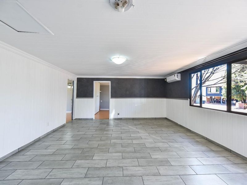 A spacious, empty living area featuring modern grey tiled flooring, white timber wall paneling, and a wall-mounted split-system air conditioner.
