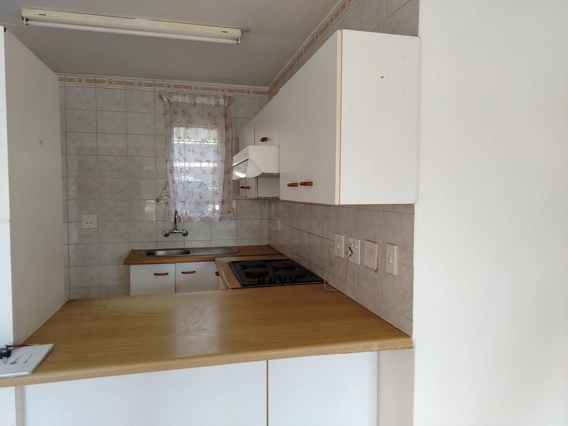 A compact kitchen featuring built-in cabinetry, laminate countertops, an electric hob, and a tiled backsplash, offering a functional layout ready for modernization.