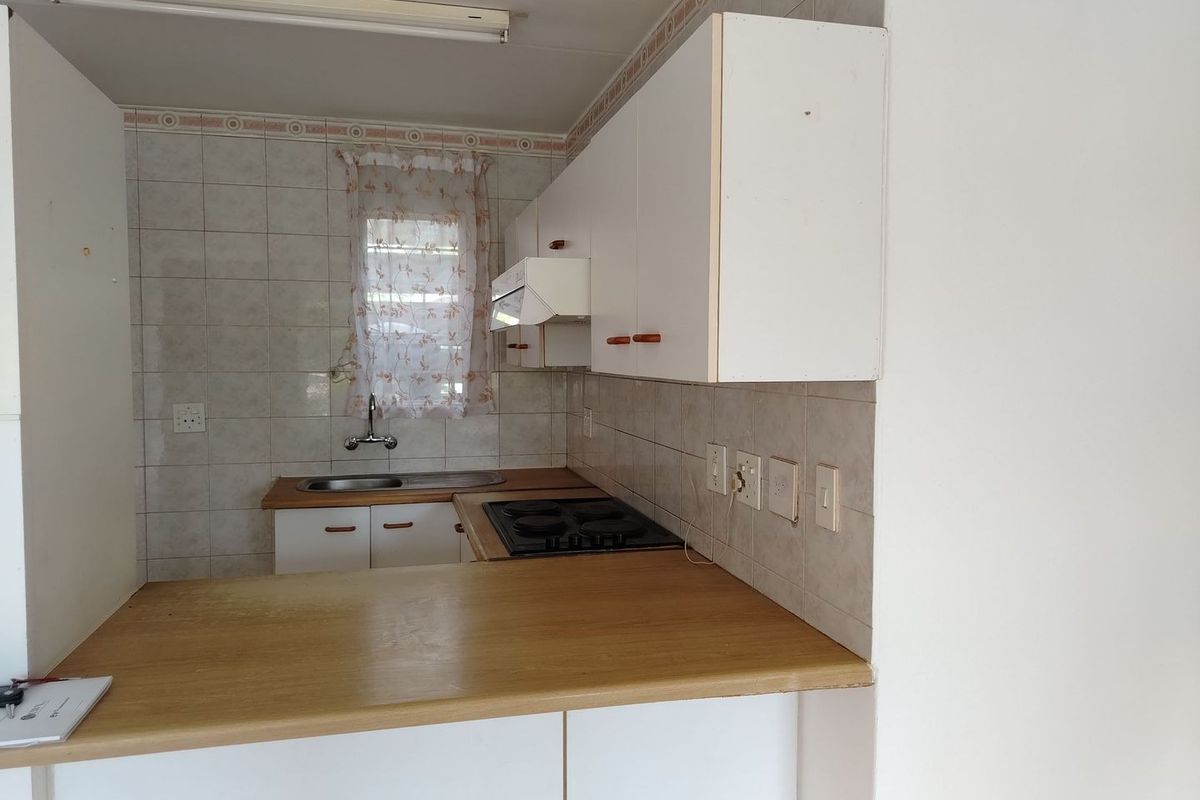 A compact kitchen featuring built-in cabinetry, laminate countertops, an electric hob, and a tiled backsplash, offering a functional layout ready for modernization.