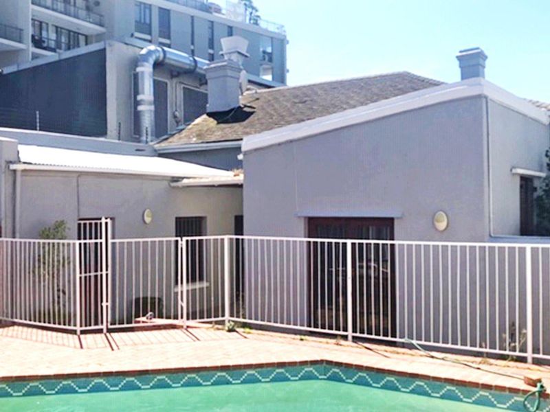 A view of the rear exterior featuring a swimming pool with brick coping and a white metal safety fence against the house facade.