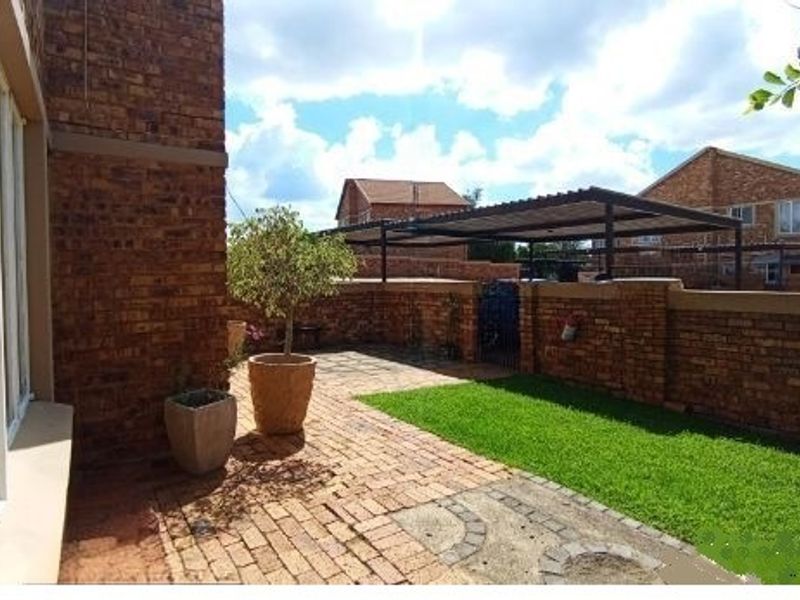 A private rear courtyard featuring a brick-paved patio, a small lawn area, and a covered carport structure.
