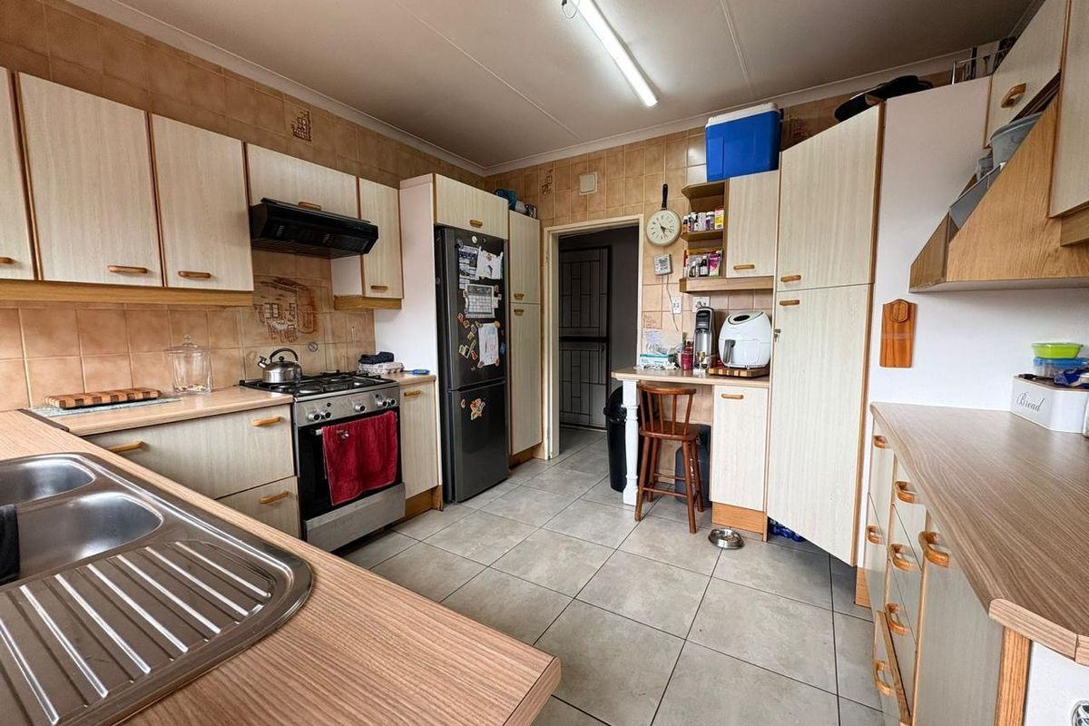 A functional kitchen featuring wood-look laminate cabinetry, tiled flooring, a gas stove with extractor fan, and a double stainless steel sink.