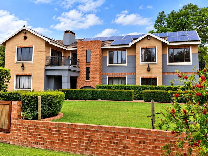 A well-maintained double-story brick residence featuring solar panels, a balcony with iron railings, and a neat front garden with a brick boundary wall.